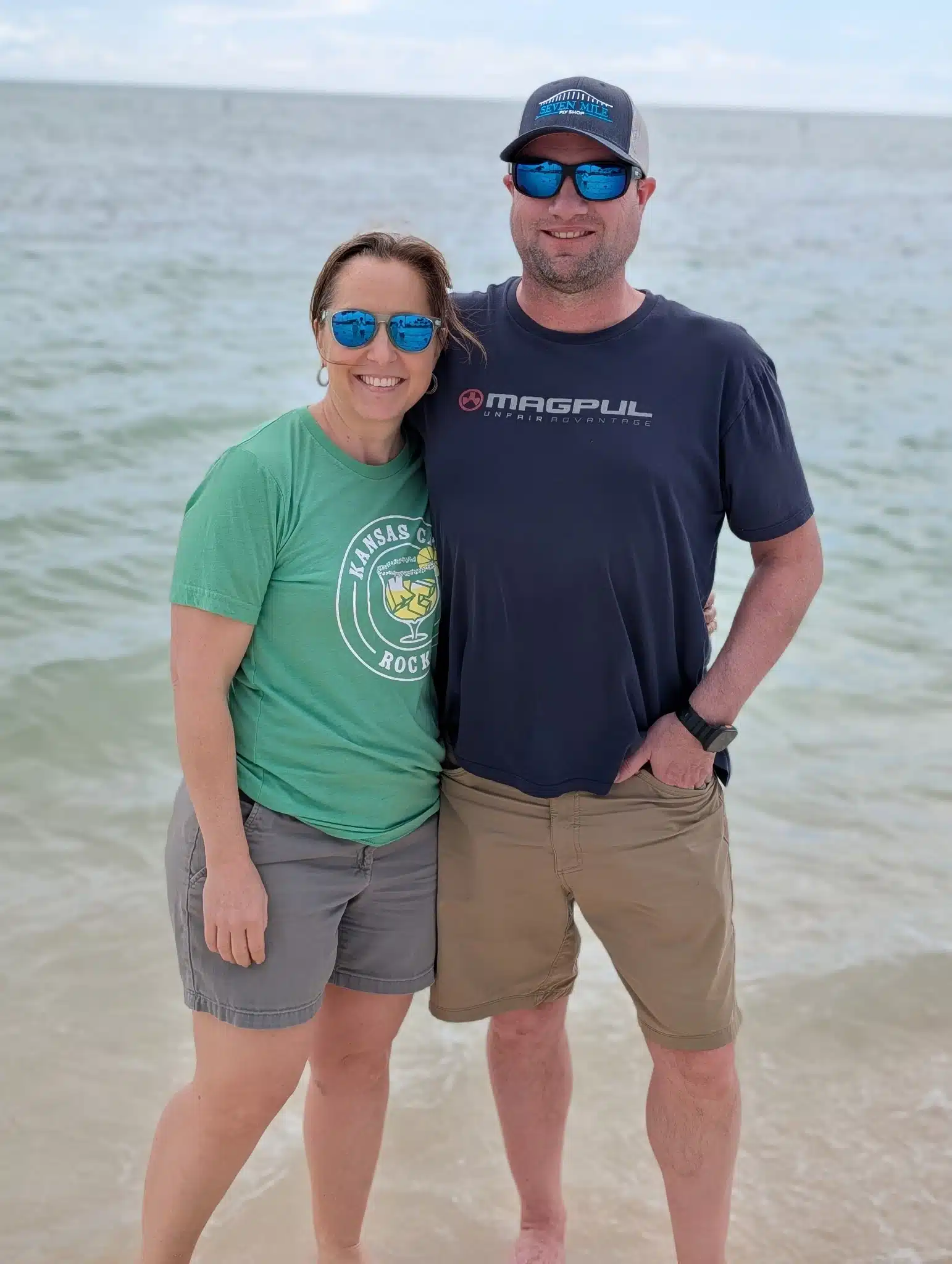 My husband and I smiling together on the beach in Florida during our family vacation, standing in front of calm ocean water.